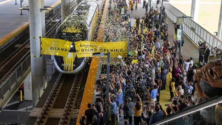 It took the better part of a decade to make it happen, but high-speed Brightline trains are whisking passengers daily from Miami to Orlando, adding a travel option that vacationers and business commuters over the years rarely thought possible. Now, the Miami-based company is turning its attention to a variety of next steps — ranging from helping Miami-Dade, Broward and Palm Beach counties eventually install commuter service in their regions, and to expanding the regional rail line from Orlando to Tampa on the Gulf Coast. In its latest monthly report to bondholders who support the multi-billion dollar passenger railroad, management sounded an upbeat chord with the initial public response to the Orlando extension, as well as the growing sustainability of the South Florida service, which started in 2018. “The addition of long-distance service has fundamentally transformed our business, with average fares, ancillary revenue per passenger and ridership all increasing significantly,” the company said in its report for November. “Results to date are strong and accelerating, with 190,448 customers trying our long distance service in its first 70 days of operation through November 30.” Playlist Error: This content is currently unavailable from within your country. Customers, the report says, are buying into a Miami-Orlando fare structure of $79 one-way for its economy level SMART tickets ($199 for a family of four) and $149 for its upper level PREMIUM service. “The market has shown a willingness to pay these prices and we have been able to yield fares higher for peak trains,” the report says of a “highly diverse” customer base that includes Florida residents, domestic U.S. visitors, and international travelers from 92 countries. The company has cut 349 “business-to-business” corporate deals “with some of the most notable employers in Florida” from industries that include “banking/finance, legal firms, restaurant/hospitality, tech, and real estate development.” “We have also begun executing contracts with major airlines to support airline staff movement between their key locations in Florida and are evaluating passenger recovery agreement opportunities with certain airlines,” the report said. Ambitious goals, wide acceptance Those steady streams of business are important for a private enterprise that intends to refinance billions in debt that funded its startup phase, and envisions another major expansion project to Tampa while developing a separate commuter service with South Florida’s three major counties. Nationally, Brightline is being held aloft by high-speed rail advocates as a template for regional projects elsewhere, including the company’s own Brightline West, which in early December received a $3 billion lift from Washington to help build a new line between Las Vegas and the Los Angeles area. Locally, the results have economic development promoters waxing positive about what Brightline has done for them thus far. And regions that have yet to obtain station stops for their localities are pining for a piece of the action. In Palm Beach County, it has played a role in buttressing the area’s desire to be a magnet for corporate headquarters and new businesses in the fields of life sciences and finance. “Florida’s enhanced connectivity through the Brightline has transformed the landscape, making it an enticing hub for statewide business endeavors,” Kelly Smallridge, president and CEO of the Business Development Board in Palm Beach County, said in a statement to the South Florida Sun Sentinel last week. “Palm Beach County’s recognition as ‘Wall Street South’ coupled with multiple stations across key city centers, has drawn a surge of affluent individuals to the area, contributing significantly to Brightline’s use among executives seeking seamless travel or cross-county professional engagements.” Shortly after the railroad’s 170-mile extension became active in September between West Palm Beach and Orlando, a delegation of rail-hungry political and business officials from the Tampa area visited South Florida to see what Brightline can offer. “It’s just incredible what Brightline has done for South and Central Florida, and we can’t wait to get it into the Tampa Bay area,” Tampa Mayor Jane Castor told reporters. According to the November financial report and other public statements, here is a look at long-term projects that Brightline intends to continue working on in the coming year: South Florida Commuter Development Comment: “Miami-Dade and Broward Counties continue to advance projects to provide commuter service on our corridor, improving mobility access for local neighborhoods and acting as a feeder system to our intercity service,” the report said. “These plans would include extending existing commuter service onto and along Brightline’s corridor.” Status: Broward County has $173 million of the estimated $323 million project planned and-or committed, according to the report. The county has completed a package to seek money from the Federal Capital Investment Grant Small Starts program. The Florida Department of Transportation has been driving a multi-year study process for a Broward Commuter South line south of the New River, as well as for points into northern Broward and Palm Beach counties. But a heated battle between the county and the City of Fort Lauderdale over an improved New River crossing downtown has raised concerns among other cities over a potential delay in the commuter line’s northward development. Currently, an aging drawbridge serves as the only means for carrying daily passenger trains operated by Brightline and freight trains run by the Florida East Coast Railway. A new commuter service would add to the existing bridge’s burden. A Brightline train takes the Florida East Coast Railway bridge over the New River in downtown Fort Lauderdale on Dec. 7. (Joe Cavaretta/South Florida Sun Sentinel) A Brightline train passes over the FEC bridge at the New River in downtown Fort Lauderdale. The crossing’s future overhaul holds the key to a new commuter line to be developed by Broward County in concert with Brightline, which holds access rights to the rail corridor. (Joe Cavaretta/South Florida Sun Sentinel file) County commissioners have opted for a new bridge. Fort Lauderdale Mayor Dean Trantalis and a cadre of local business leaders have been campaigning for a tunnel, arguing that another above-ground span would divide the city and disrupt further development in the area. Cities including Oakland Park, Pompano Beach and Deerfield Beach have all been designated by the DOT as potential stops for the service. .And local planners are including stations in their urban redevelopment programs. Palm Beach County is waiting in the wings, having penciled local commuter rail service into its transportation development plans. Miami-Dade has $294 million of the estimated $578 million project committed from the county and state of Florida, according to the report. The final project funding component is expected to be provided by the Federal Capital Investment Grant New Starts program after Miami-Dade completes the engineering phase. The county obtained environmental permitting approval for the project in November. Stations: In Broward, state DOT planners and the county have initially agreed on stations for Hollywood, Fort Lauderdale Hollywood International Airport and a neighborhood near the Broward Health hospital south of the New River. In Miami-Dade, five stations would be built between Aventura and the Brightline MiamiCentral station. In Palm Beach County, three commuter stations between Boca Raton and West Palm Beach and three others would be built “between West Palm Beach and Jupiter,” according to the Brightline financial report. Although Brightline is working with the counties to develop their commuter projects, all of which will yield millions in annual access fees to the railroad, it is likely that another yet-to-be-determined entity would be the operator. Treasure, Space Coasts Comment: “With the extension to Orlando now in operation and given the success of our Aventura and Boca Raton stations, we are reviewing and developing options for additional future in-line stations,” according to the November report.. “Likely stations include one expected to be located in Brevard County and another to be located along Florida’s Treasure Coast north of West Palm Beach.” Stations: Along the Treasure Coast, Stuart and Fort Pierce are expressing strong interest. When the company’s inaugural train made its way to Orlando in late September, Stuart officials organized a trackside welcoming committee complete with banners and a salutary hosing of the passenger cars by a fire truck as the train passed through town. Status: The selection process is in its early stages as Brightline recently issued a call for applications from public and private landowners. The deadline for submission was Dec. 22. “We’ll start the process of evaluating those applications and be in a position to make a selection and work through agreements in the first quarter,” spokesman Ben Porritt said by email last week. A Treasure Coast station could be open at some point in 2028. But any station to the north in Brevard is not likely to come fruition for quite some time. Although Brightline’s report alludes to the potential for one in the county, there are no provisions mentioned for funding. Tampa Mayor Jane Castor and West Palm Beach Mayor Keith James speak during a tour of the West Palm Beach Brightline Station on Monday, Nov. 6, 2023. (Amy Beth Bennett / South Florida Sun Sentinel) Tampa Mayor Jane Castor visits with West Palm Beach Mayor Keith James as the mayor led a delegation of Tampa Bay area officials on a tour of the West Palm Beach Brightline station in early November. (Amy Beth Bennett / South Florida Sun Sentinel file) Orlando-Tampa Comment: “Our planned Tampa extension is expected to include stops at the Orange County Convention Center and South International Drive and connect to an expanded SunRail commuter system,” according to Brightline’s November report. “These stops would provide convenient access to Central Florida business destinations and major theme parks and resorts including SeaWorld Orlando, Universal Orlando Resort and the Walt Disney World Resort, among others.” Status: “It is complex to get to Tampa, but we’re up to the challenge,” Christine Kefauver, senior vice president of corporate development for Brightline, recently told the Florida House Transportation and Modals Subcommittee. According to the News Service of Florida, she said the company has been involved in the “Sunshine Corridor conversation for about two years, and we really do see us making tremendous strides on that coming up soon.” Stations: In Tampa, to be determined. “In connection with the planned overall refinancing of the company, we intend to sell or otherwise confer the assets, rights and obligations related to the Orlando-Tampa Project to an affiliate for future development of additional stations,” the Brightline report says.