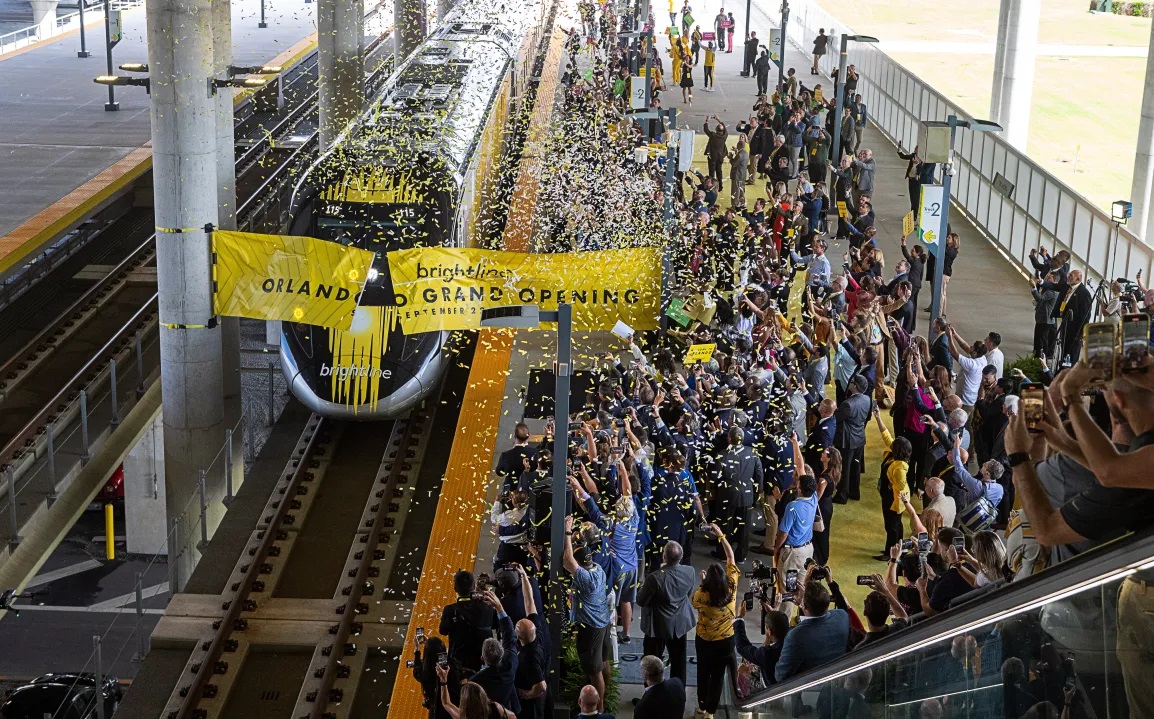 It took the better part of a decade to make it happen, but high-speed Brightline trains are whisking passengers daily from Miami to Orlando, adding a travel option that vacationers and business commuters over the years rarely thought possible. Now, the Miami-based company is turning its attention to a variety of next steps — ranging from helping Miami-Dade, Broward and Palm Beach counties eventually install commuter service in their regions, and to expanding the regional rail line from Orlando to Tampa on the Gulf Coast. In its latest monthly report to bondholders who support the multi-billion dollar passenger railroad, management sounded an upbeat chord with the initial public response to the Orlando extension, as well as the growing sustainability of the South Florida service, which started in 2018. “The addition of long-distance service has fundamentally transformed our business, with average fares, ancillary revenue per passenger and ridership all increasing significantly,” the company said in its report for November. “Results to date are strong and accelerating, with 190,448 customers trying our long distance service in its first 70 days of operation through November 30.” Playlist Error: This content is currently unavailable from within your country. Customers, the report says, are buying into a Miami-Orlando fare structure of $79 one-way for its economy level SMART tickets ($199 for a family of four) and $149 for its upper level PREMIUM service. “The market has shown a willingness to pay these prices and we have been able to yield fares higher for peak trains,” the report says of a “highly diverse” customer base that includes Florida residents, domestic U.S. visitors, and international travelers from 92 countries. The company has cut 349 “business-to-business” corporate deals “with some of the most notable employers in Florida” from industries that include “banking/finance, legal firms, restaurant/hospitality, tech, and real estate development.” “We have also begun executing contracts with major airlines to support airline staff movement between their key locations in Florida and are evaluating passenger recovery agreement opportunities with certain airlines,” the report said. Ambitious goals, wide acceptance Those steady streams of business are important for a private enterprise that intends to refinance billions in debt that funded its startup phase, and envisions another major expansion project to Tampa while developing a separate commuter service with South Florida’s three major counties. Nationally, Brightline is being held aloft by high-speed rail advocates as a template for regional projects elsewhere, including the company’s own Brightline West, which in early December received a $3 billion lift from Washington to help build a new line between Las Vegas and the Los Angeles area. Locally, the results have economic development promoters waxing positive about what Brightline has done for them thus far. And regions that have yet to obtain station stops for their localities are pining for a piece of the action. In Palm Beach County, it has played a role in buttressing the area’s desire to be a magnet for corporate headquarters and new businesses in the fields of life sciences and finance. “Florida’s enhanced connectivity through the Brightline has transformed the landscape, making it an enticing hub for statewide business endeavors,” Kelly Smallridge, president and CEO of the Business Development Board in Palm Beach County, said in a statement to the South Florida Sun Sentinel last week. “Palm Beach County’s recognition as ‘Wall Street South’ coupled with multiple stations across key city centers, has drawn a surge of affluent individuals to the area, contributing significantly to Brightline’s use among executives seeking seamless travel or cross-county professional engagements.” Shortly after the railroad’s 170-mile extension became active in September between West Palm Beach and Orlando, a delegation of rail-hungry political and business officials from the Tampa area visited South Florida to see what Brightline can offer. “It’s just incredible what Brightline has done for South and Central Florida, and we can’t wait to get it into the Tampa Bay area,” Tampa Mayor Jane Castor told reporters. According to the November financial report and other public statements, here is a look at long-term projects that Brightline intends to continue working on in the coming year: South Florida Commuter Development Comment: “Miami-Dade and Broward Counties continue to advance projects to provide commuter service on our corridor, improving mobility access for local neighborhoods and acting as a feeder system to our intercity service,” the report said. “These plans would include extending existing commuter service onto and along Brightline’s corridor.” Status: Broward County has $173 million of the estimated $323 million project planned and-or committed, according to the report. The county has completed a package to seek money from the Federal Capital Investment Grant Small Starts program. The Florida Department of Transportation has been driving a multi-year study process for a Broward Commuter South line south of the New River, as well as for points into northern Broward and Palm Beach counties. But a heated battle between the county and the City of Fort Lauderdale over an improved New River crossing downtown has raised concerns among other cities over a potential delay in the commuter line’s northward development. Currently, an aging drawbridge serves as the only means for carrying daily passenger trains operated by Brightline and freight trains run by the Florida East Coast Railway. A new commuter service would add to the existing bridge’s burden. A Brightline train takes the Florida East Coast Railway bridge over the New River in downtown Fort Lauderdale on Dec. 7. (Joe Cavaretta/South Florida Sun Sentinel) A Brightline train passes over the FEC bridge at the New River in downtown Fort Lauderdale. The crossing’s future overhaul holds the key to a new commuter line to be developed by Broward County in concert with Brightline, which holds access rights to the rail corridor. (Joe Cavaretta/South Florida Sun Sentinel file) County commissioners have opted for a new bridge. Fort Lauderdale Mayor Dean Trantalis and a cadre of local business leaders have been campaigning for a tunnel, arguing that another above-ground span would divide the city and disrupt further development in the area. Cities including Oakland Park, Pompano Beach and Deerfield Beach have all been designated by the DOT as potential stops for the service. .And local planners are including stations in their urban redevelopment programs. Palm Beach County is waiting in the wings, having penciled local commuter rail service into its transportation development plans. Miami-Dade has $294 million of the estimated $578 million project committed from the county and state of Florida, according to the report. The final project funding component is expected to be provided by the Federal Capital Investment Grant New Starts program after Miami-Dade completes the engineering phase. The county obtained environmental permitting approval for the project in November. Stations: In Broward, state DOT planners and the county have initially agreed on stations for Hollywood, Fort Lauderdale Hollywood International Airport and a neighborhood near the Broward Health hospital south of the New River. In Miami-Dade, five stations would be built between Aventura and the Brightline MiamiCentral station. In Palm Beach County, three commuter stations between Boca Raton and West Palm Beach and three others would be built “between West Palm Beach and Jupiter,” according to the Brightline financial report. Although Brightline is working with the counties to develop their commuter projects, all of which will yield millions in annual access fees to the railroad, it is likely that another yet-to-be-determined entity would be the operator. Treasure, Space Coasts Comment: “With the extension to Orlando now in operation and given the success of our Aventura and Boca Raton stations, we are reviewing and developing options for additional future in-line stations,” according to the November report.. “Likely stations include one expected to be located in Brevard County and another to be located along Florida’s Treasure Coast north of West Palm Beach.” Stations: Along the Treasure Coast, Stuart and Fort Pierce are expressing strong interest. When the company’s inaugural train made its way to Orlando in late September, Stuart officials organized a trackside welcoming committee complete with banners and a salutary hosing of the passenger cars by a fire truck as the train passed through town. Status: The selection process is in its early stages as Brightline recently issued a call for applications from public and private landowners. The deadline for submission was Dec. 22. “We’ll start the process of evaluating those applications and be in a position to make a selection and work through agreements in the first quarter,” spokesman Ben Porritt said by email last week. A Treasure Coast station could be open at some point in 2028. But any station to the north in Brevard is not likely to come fruition for quite some time. Although Brightline’s report alludes to the potential for one in the county, there are no provisions mentioned for funding. Tampa Mayor Jane Castor and West Palm Beach Mayor Keith James speak during a tour of the West Palm Beach Brightline Station on Monday, Nov. 6, 2023. (Amy Beth Bennett / South Florida Sun Sentinel) Tampa Mayor Jane Castor visits with West Palm Beach Mayor Keith James as the mayor led a delegation of Tampa Bay area officials on a tour of the West Palm Beach Brightline station in early November. (Amy Beth Bennett / South Florida Sun Sentinel file) Orlando-Tampa Comment: “Our planned Tampa extension is expected to include stops at the Orange County Convention Center and South International Drive and connect to an expanded SunRail commuter system,” according to Brightline’s November report. “These stops would provide convenient access to Central Florida business destinations and major theme parks and resorts including SeaWorld Orlando, Universal Orlando Resort and the Walt Disney World Resort, among others.” Status: “It is complex to get to Tampa, but we’re up to the challenge,” Christine Kefauver, senior vice president of corporate development for Brightline, recently told the Florida House Transportation and Modals Subcommittee. According to the News Service of Florida, she said the company has been involved in the “Sunshine Corridor conversation for about two years, and we really do see us making tremendous strides on that coming up soon.” Stations: In Tampa, to be determined. “In connection with the planned overall refinancing of the company, we intend to sell or otherwise confer the assets, rights and obligations related to the Orlando-Tampa Project to an affiliate for future development of additional stations,” the Brightline report says.